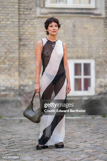 Alyssa Coscarelli wears a silver oversized heart pendant necklace, a black and white striped print pattern transparent / sleeveless / long dress, a...