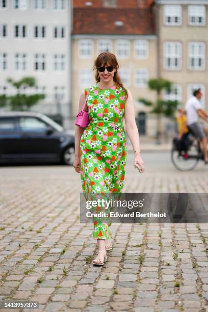 Erin Fitzpatrick wears black sunglasses, a neon green with pink / white / blue / orange flower print pattern / sleeveless / long maxi dress, a pink...
