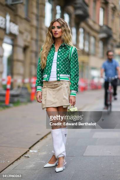 Emili Sindlev wears gold earrings, a white V-neck tank-top, a green with white embossed LV pattern buttoned jacket from Louis Vuitton, a beige...