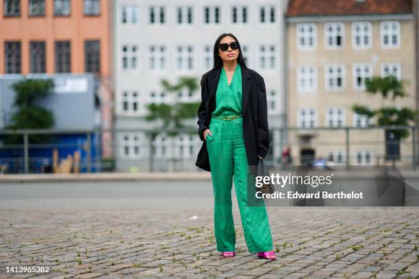 Miki Cheung wears black sunglasses, gold earrings, a green V-neck silk blouse, matching green silk large pants, a gold logo metallic belt from Fendi,...