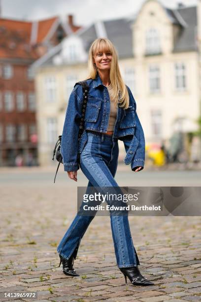 Jeanette Madsen wears a beige ribbed halter-neck / cropped tank-top, a navy blue denim buttoned / cropped jacket, high waist matching bicolored denim...