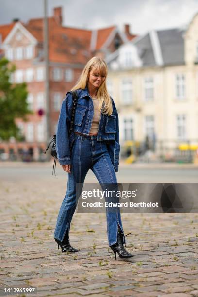 Jeanette Madsen wears a beige ribbed halter-neck / cropped tank-top, a navy blue denim buttoned / cropped jacket, high waist matching bicolored denim...