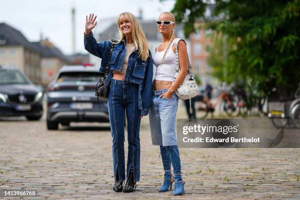Jeanette Madsen wears a beige ribbed halter-neck / cropped tank-top, a navy blue denim buttoned / cropped jacket, high waist matching bicolored denim...