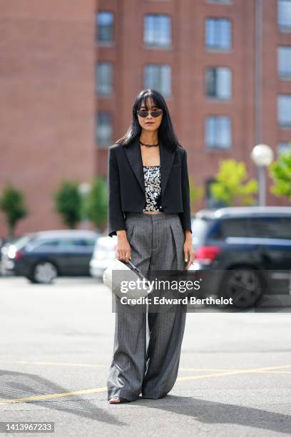 Pornwika Spiecker wears black cat eyes sunglasses, a black chain necklace, a black with embroidered silver sequined V-neck t-shirt, a black cropped...