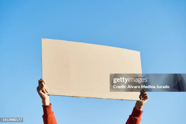 unrecognizable woman's hands holding a protest banner with no message, with the sky in the background. - sign fotografías e imágenes de stock