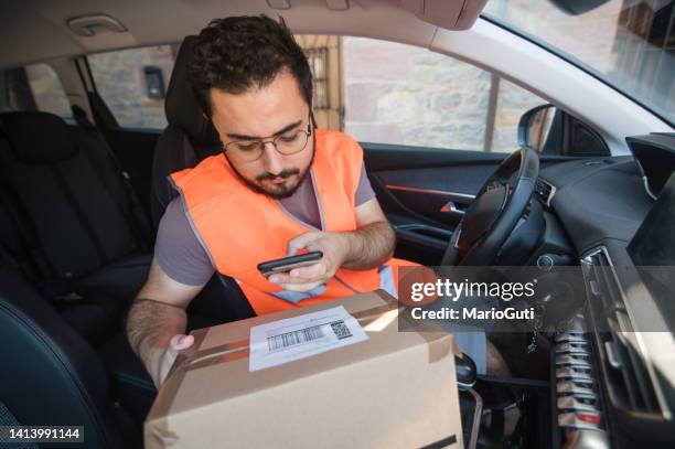 delivery man scanning a package tag with a smart phone - postbode stockfoto's en -beelden