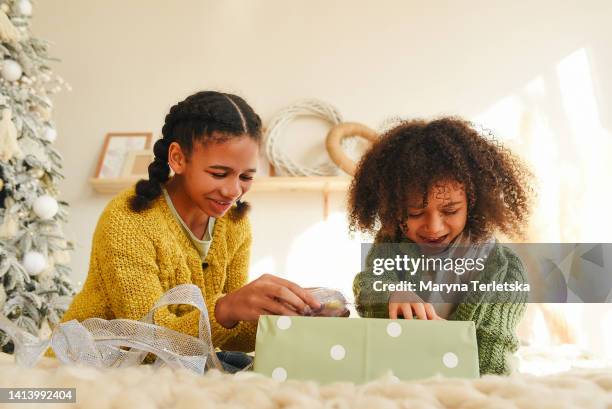 two afro sisters sit on a large bed and open a gift. room design in light colors. christmas mood. christmas presents. - open day 4 stock pictures, royalty-free photos & images