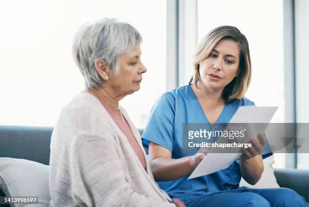 nurse showing test results to senior woman on paper and talking, discussing and sharing treatment options in old age home. caregiver, caretaker or medical healthcare professional helping elderly lady - doctor and patient talking imagens e fotografias de stock