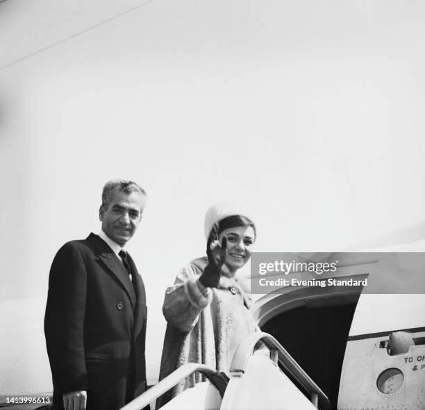 Iranian Royals Mohammad Reza Pahlavi , Shah of Iran, and his wife, Farah Pahlavi, Shahbanu of Iran, turn and smile, with Farah waving, as they board...