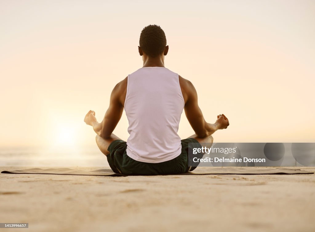 Fit and active man doing yoga, meditating and relaxation exercise on the beach. Calm, peaceful and relaxed male doing breathing exercises and practicing mindfulness by the seashore during sunrise