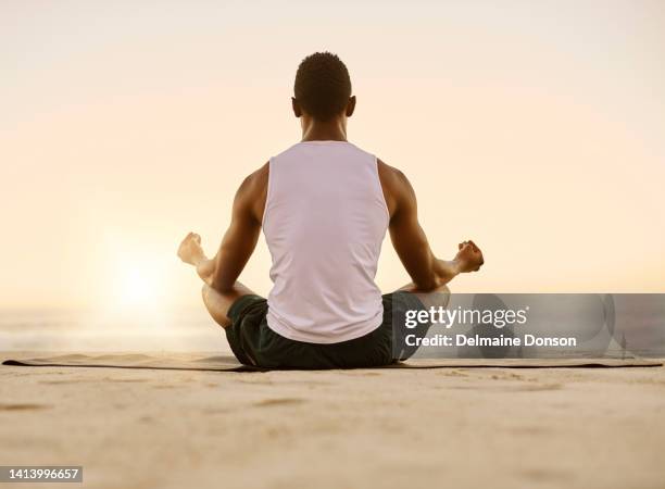 fit and active man doing yoga, meditating and relaxation exercise on the beach. calm, peaceful and relaxed male doing breathing exercises and practicing mindfulness by the seashore during sunrise - zen man stock pictures, royalty-free photos & images