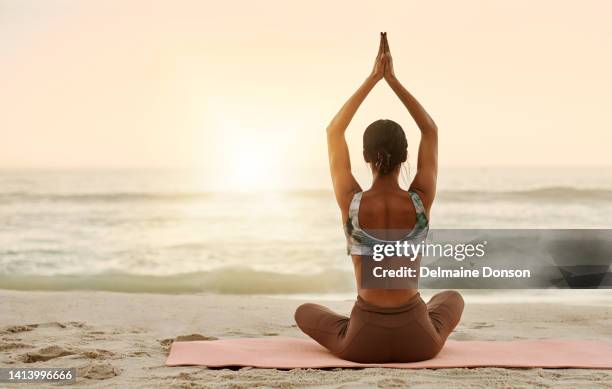 relaxed, zen and healthy woman meditating on beach with arms raised in prayer pose and sitting legs crossed by sea or ocean. calm, serene or peaceful yogi in holistic yoga breathing for mental health - namaste stock pictures, royalty-free photos & images