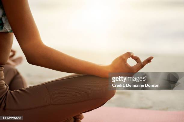 achtsame, ruhige und entspannte frau, die im freien am strand meditiert und in der lotusposition sitzt. nahaufnahme einer fitten und zen-frau, die während des sonnenaufgangs draußen am meer oder am meeresufer yoga macht - mudra stock-fotos und bilder