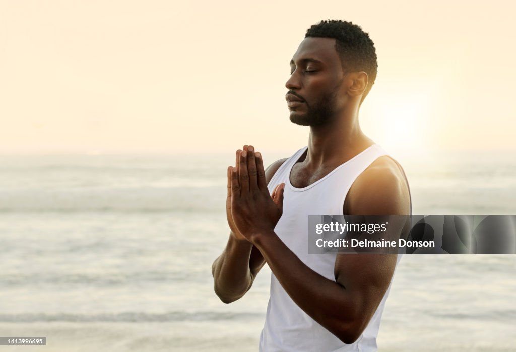 Calm and spiritual man praying or meditating on beach with sunset sky copy space background. One zen guy practicing yoga Anjali mudra, namaste, prayer hands with palms together for healthy lifestyle