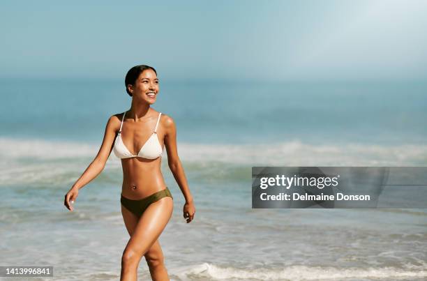 fittes, schönes und durchtrainiertes bikini-model am strand, das spaß und erholsamen sommerurlaub am meer und meer genießt, während sie einen badeanzug tragen. lächelnde, glückliche und wandelnde frau in bademode im tropischen urlaub - badebekleidung stock-fotos und bilder