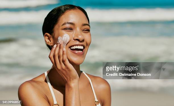 young woman applying sun lotion to her face for protection from uv while having fun at the beach outside on vacation. beautiful african female with natural and perfect skin using her hands spf cream - cream for face stock pictures, royalty-free photos & images