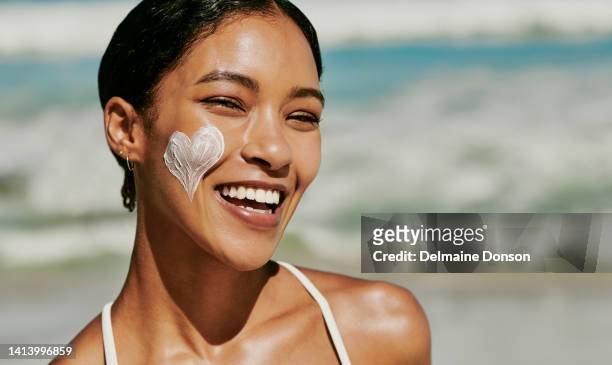 smiling and happy woman with sunscreen, sunblock cream and protection product on face in heart shape. portrait of young female with skincare to protect from the sun enjoying a beach vacation - face happy sun stockfoto's en -beelden