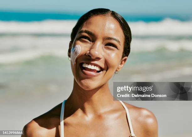 hautpflege, spaß und eine glückliche schwarze frau, die am strand sonnencreme aufträgt. lächelnde schwarze frau, die sonnencreme benutzt, um ihre haut vor der sommersonne zu schützen. dame, die einen tropischen urlaub am meer genießt - woman skin face stock-fotos und bilder