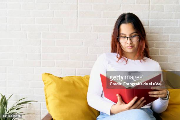 horizontal shot of teen girl enjoying reading a red book at backyard - teenager reading a book stock pictures, royalty-free photos & images