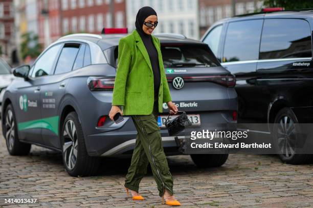 Guest wears black sunglasses from Marine Serre, black scarf, a black ribbed high neck / long sleeves t-shirt, a green ribbed velvet blazer jacket,...