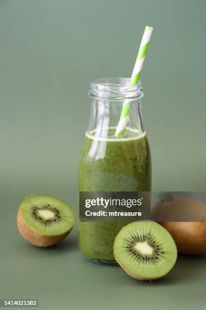 immagine ravvicinata di vetro, bottiglia con tappo a vite di frullato di succo di frutta e verdura verde con cannuccia spogliata, mela, kiwi, broccoli, cetriolo e succo di lime, pezzi interi e dimezzati di kiwi, sfondo verde, focus sul primo piano - kiwi foto e immagini stock