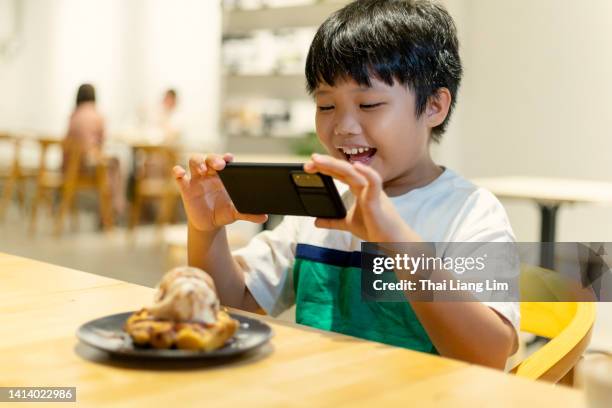 un garçon utilisant un smartphone prenant des photos de son dessert dans un restaurant - child foodie photos et images de collection