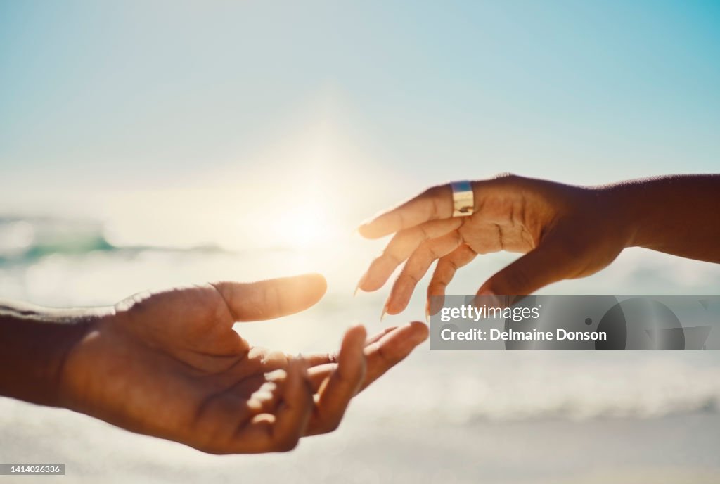 Amore e cura gesto della mano con la coppia che raggiunge un tocco delicato sul cielo blu e sullo sfondo della spiaggia con spazio di copia. Due mani innamorate quasi a toccarsi come simbolo o segno di romanticismo e unità
