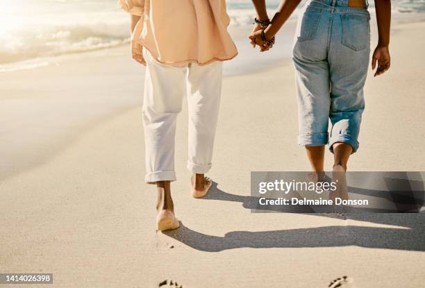 closeup couple walking barefoot on a sandy beach and enjoying fresh air together on vacation. low view of husband and wife taking a slow, romantic walk while holding hands while on summer holiday - slow stock pictures, royalty-free photos & images