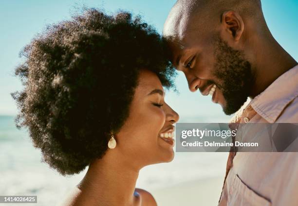 happy, smiling and cheerful african couple bonding, feeling in love or enjoying summer break together on beach by sea or ocean. closeup headshot of afro woman standing close to relaxed man on holiday - hair love 個照片及圖片檔