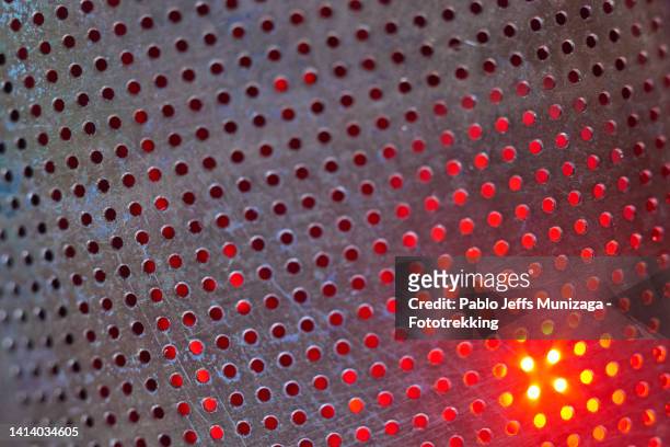 perforated steel plate with flash of red color - geperforeerd stockfoto's en -beelden