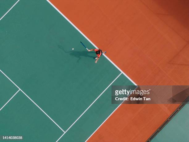 drohnen-standpunkt asiatische indische tennisspielerin serviert den ball beim üben auf dem tennisplatz direkt darüber - tennis court top view stock-fotos und bilder