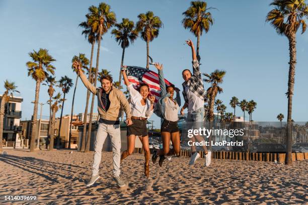 group of happy friends jumping holding an american flag. - california beach stock pictures, royalty-free photos & images