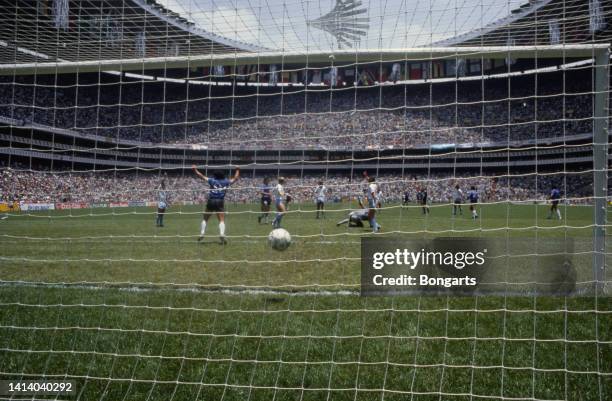 From behind the goal net, Argentine professional football player Diego Armando Maradona arms in the air in celebration after scoring one of the goals...