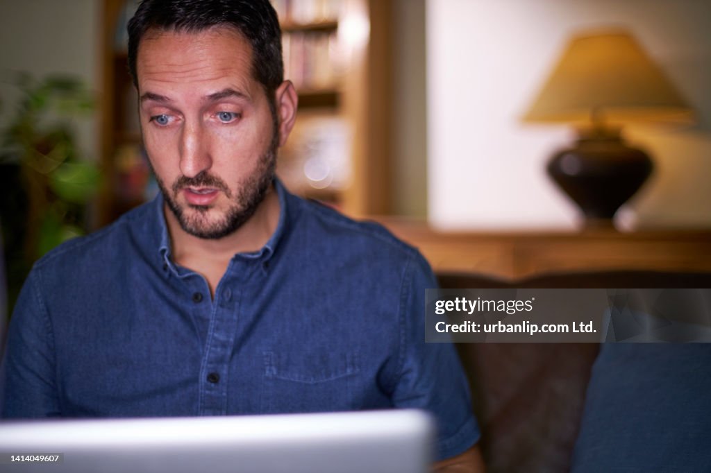 Man at home expressing shock when looking at laptop screen
