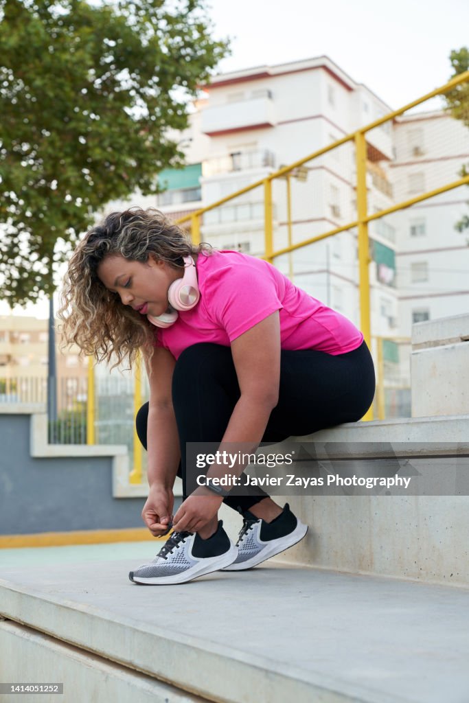Latin woman with large build tying shoe laces getting ready for jogging outdoors in the city