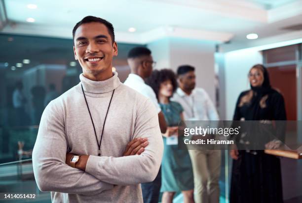a proud and happy male business leader standing arms crossed in an office. portrait of a confident intern or trainee smiling after a great working day. satisfied businessman in the creative workplace - executive board extraordinary assembly stock pictures, royalty-free photos & images