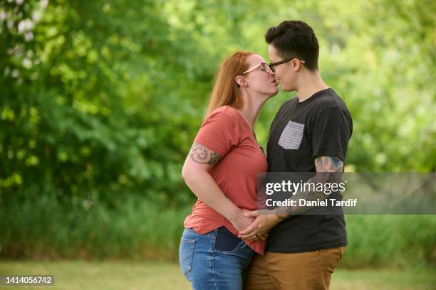 same sex couple embracing outdoors, one partner is pregnant. - photos of lesbians kissing stock pictures, royalty-free photos & images