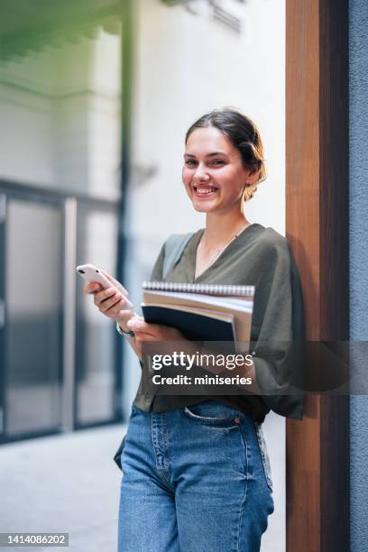 portrait of a beautiful young woman leaning against the wall holding notebooks and coffee - read book outside young woman stock pictures, royalty-free photos & images