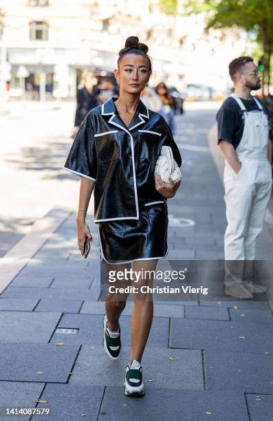 Guest is seen wearing black vinyl shirt, mini skirt, white bag outside MWorks during Copenhagen Fashion Week Spring/Summer 2023 on August 10, 2022 in...