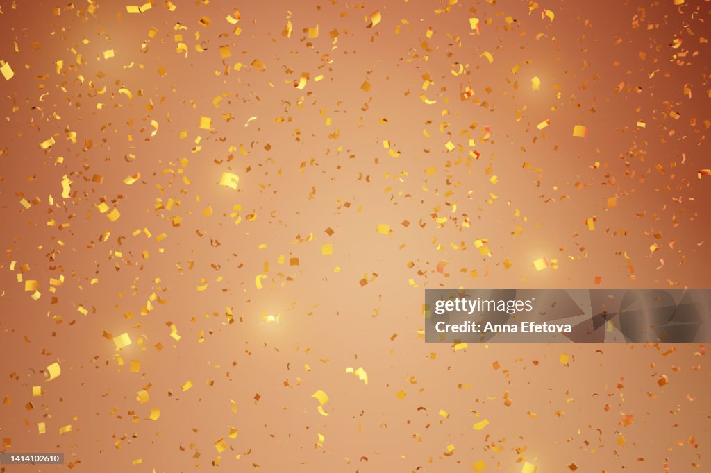 Many flying golden confetti on beige background. Festive backdrop for your products presentation. Copy space for your design. Merry Christmas and Happy New Year celebration concept