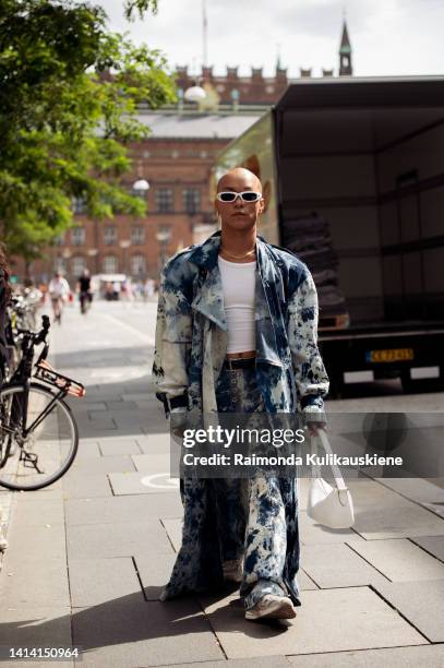 Guest wearing wide blue jenas and long denim coat posing outside Raeburn show during Copenhagen Fashion Week Spring/Summer 2023 on August 09, 2022 in...