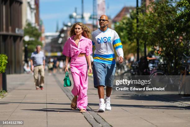 Emili Sindlev wears diamonds and gold earrings, a pink oversized short sleeves cropped shirt, matching pink large wide legs pants, a green grained...