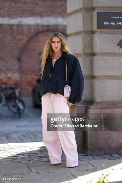 Emili Sindlev wears a gold and diamonds earrings, a pink suede with a silver large heart pendant necklace, a black oversized / puffy long sleeves /...