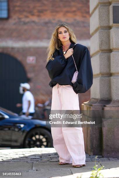 Emili Sindlev wears a gold and diamonds earrings, a pink suede with a silver large heart pendant necklace, a black oversized / puffy long sleeves /...