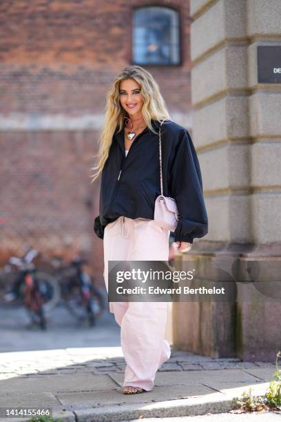 Emili Sindlev wears a gold and diamonds earrings, a pink suede with a silver large heart pendant necklace, a black oversized / puffy long sleeves /...