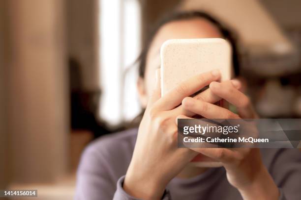 technological progress or social media problem: young mixed-race female holding smart phone up to face - obscured face phone stock pictures, royalty-free photos & images