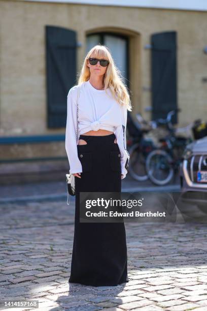 Jeanette Madsen wears black sunglasses, a gold large chain necklace, a white long sleeves with black print pattern / knot waist t-shirt, a black...
