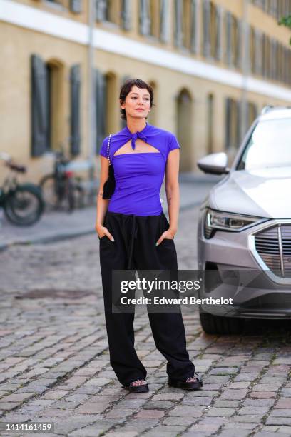 Alyssa Coscarelli wears a neon purple high neck / cut-out chest / sort sleeves t-shirt, a black velvet shoulder bag, high waist black puffy pants,...