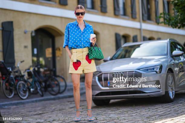 Marianne Theodorsen wears black plastic and purple velvet sunglasses from Chanel, multicolored earrings, a blue with white polka dots print pattern...