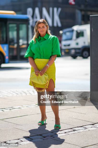 Janka Polliani wears cat eyes glasses, gold earrings, a neon green short sleeves / oversized shirt, a yellow fishnet / mesh slit short skirt, a...